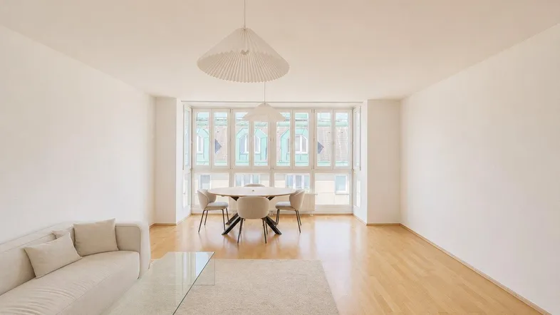 Helles Wohn- und Esszimmer mit Parkettboden, bequemer Couch und großzügigen Fenstern.