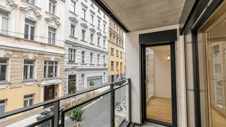 Moderner Balkon mit Glasgeländer und Blick auf die belebte Stadtstraße und historische Gebäude.