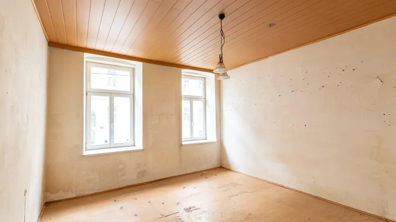 Leerer Raum mit Holzdecke und beschädigtem Holzboden, bereit für eine umfassende Renovierung.