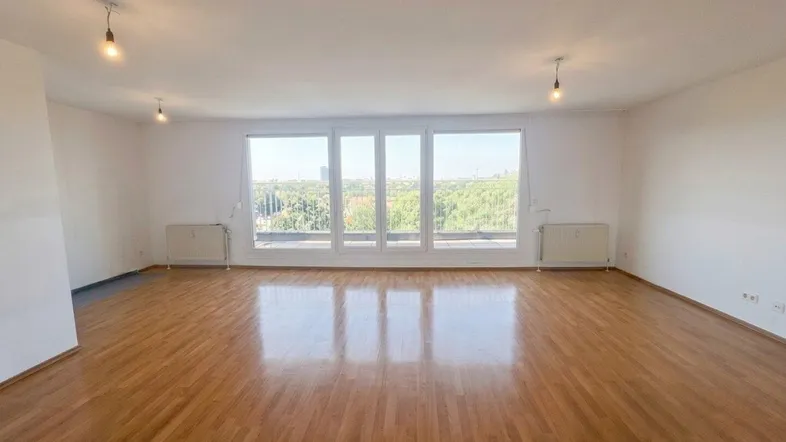Helles, leeres Wohnzimmer mit großen Fenstern, Parkettboden und weitem Blick ins Grüne.