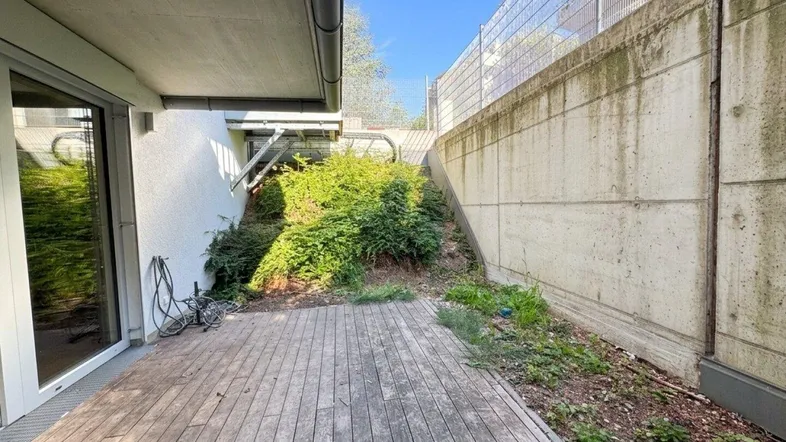 Holzterrasse im Freien mit angrenzender Bepflanzung und einer Betonmauer, die Privatsphäre bietet.