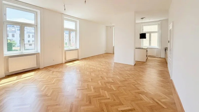 Helles, geräumiges Wohnzimmer mit Fischgrätparkett und großen Fenstern, die viel Tageslicht hereinlassen.