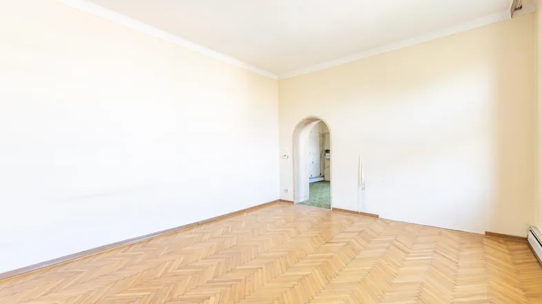 Helles, leeres Zimmer mit Fischgrätparkett und einem Rundbogen zu einem weiteren Raum.