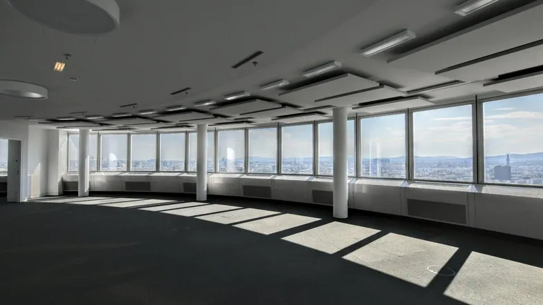 Geräumiger, moderner Büroraum mit Teppichboden, großen Fenstern und weitem Stadtblick, ideal für offene Konzepte.