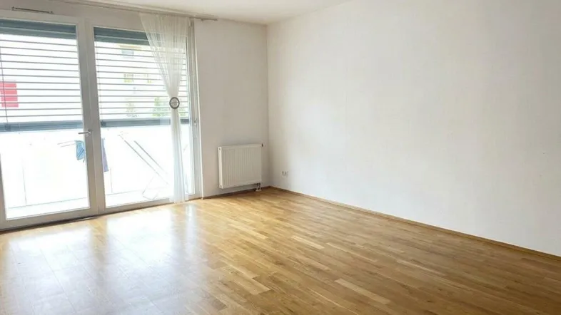 Helles, leeres Zimmer mit Parkettboden und Zugang zu einem Balkon, ideal als Wohnzimmer nutzbar.