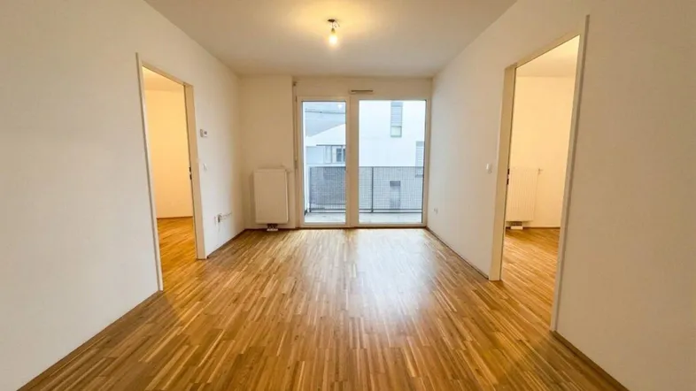 Helles Zimmer mit Parkettboden und Zugang zu einem Balkon, ideal als Wohnbereich.