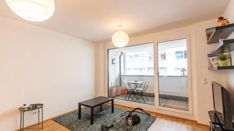Helles Wohnzimmer mit Parkettboden, Teppich und Zugang zum Balkon durch große Fenster.