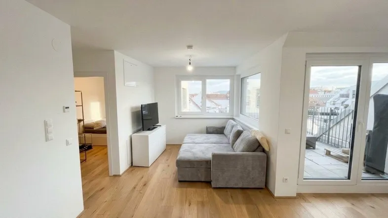 Helles Wohnzimmer mit Holzboden, Sofa und Zugang zu einer kleinen Terrasse.