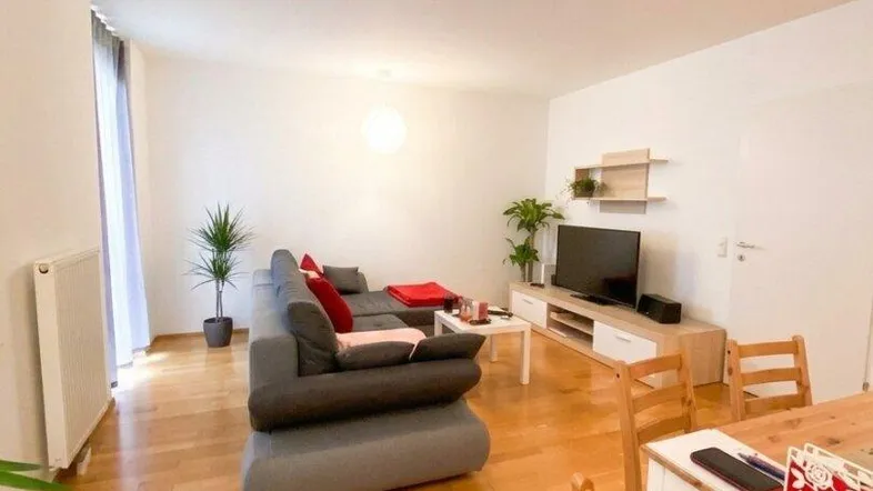 Helles Wohn- und Esszimmer mit modernem Sofa, Holztisch und Parkettboden, ideal für geselliges Beisammensein.