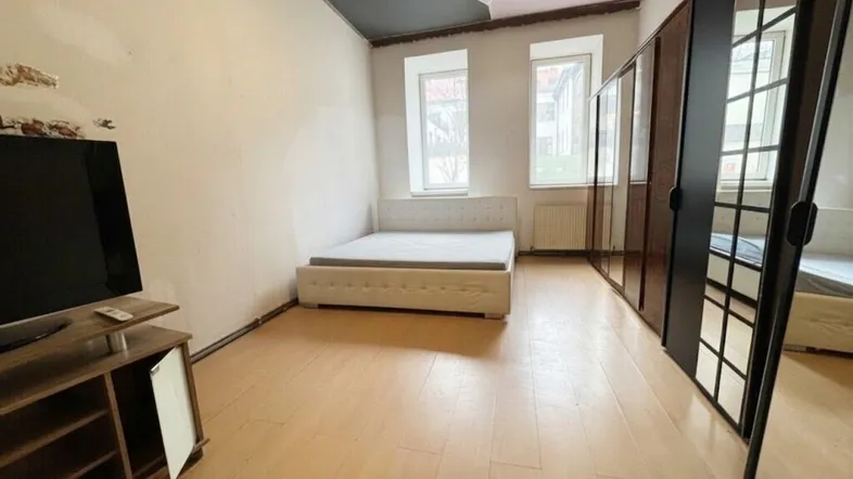 Helles Schlafzimmer mit Bett, TV-Möbel und großen Spiegelschränken, teilweise dunkler Decke.