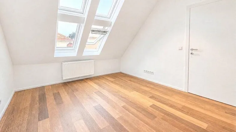 Helles Dachzimmer mit schrägen Wänden, Holzboden und zwei Dachfenstern für viel Tageslicht.