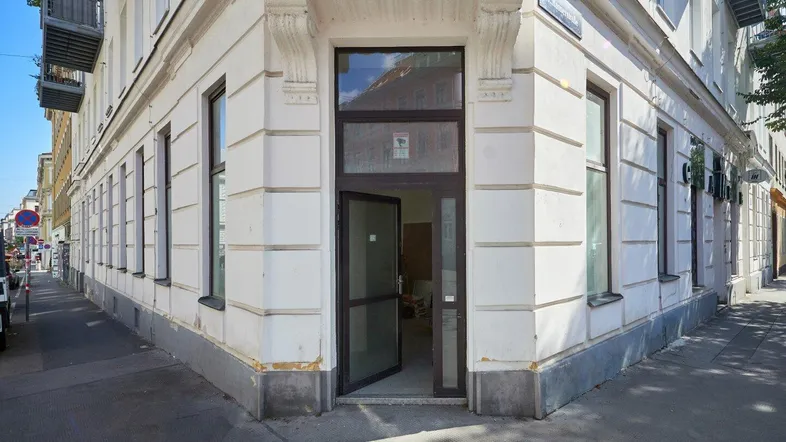 Eckgebäude mit offener Eingangstür und klassischer Fassade an einer städtischen Straße.