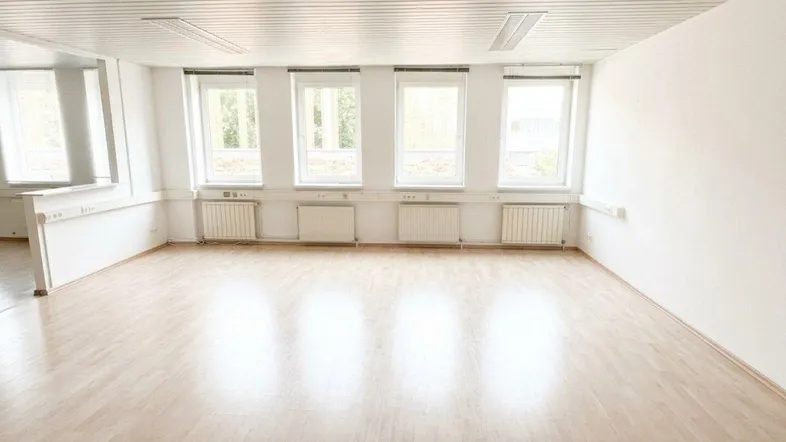 Heller Büroraum mit Holzfußboden, weißen Wänden und mehreren Fenstern für viel Tageslicht.