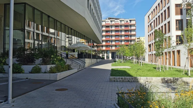 Außenansicht eines modernen Gebäudekomplexes mit gepflasterten Wegen und Grünflächen.