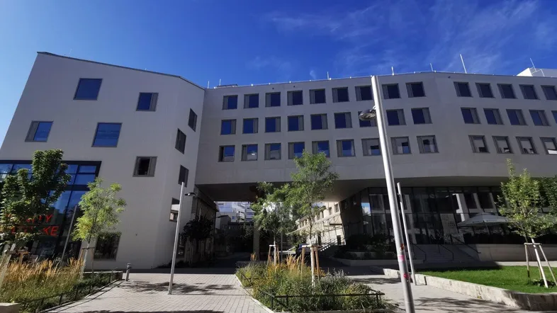 Ein modernes Bürogebäude mit markanter Architektur und großen Fensterfronten, umgeben von Grünflächen und Gehwegen.