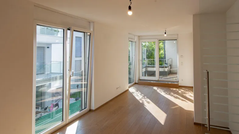 Helles Wohnzimmer mit Holzboden und großen Fenstern, die viel Tageslicht hereinlassen und Zugang zum Balkon bieten.