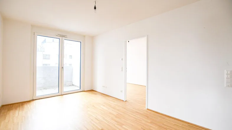 Helles Zimmer mit Parkettboden und Zugang zu einem Balkon, ideal als Wohn- oder Schlafzimmer.