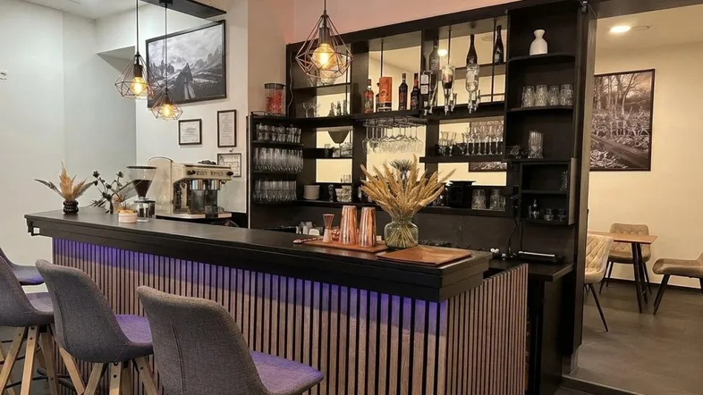 Moderne Bar mit dunkler Holztheke, beleuchteter Front und stilvollen Hängelampen, ideal für gesellige Abende.