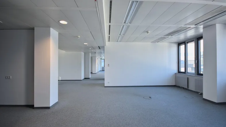 Geräumiges, leeres Büro mit Teppichboden, abgehängter Decke und großen Fenstern, bereit zur Einrichtung.