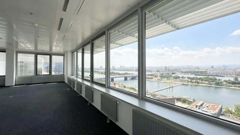 Geräumiges Büro mit Teppichboden und großen Fenstern, die einen weiten Blick auf die Stadt und den Fluss bieten.