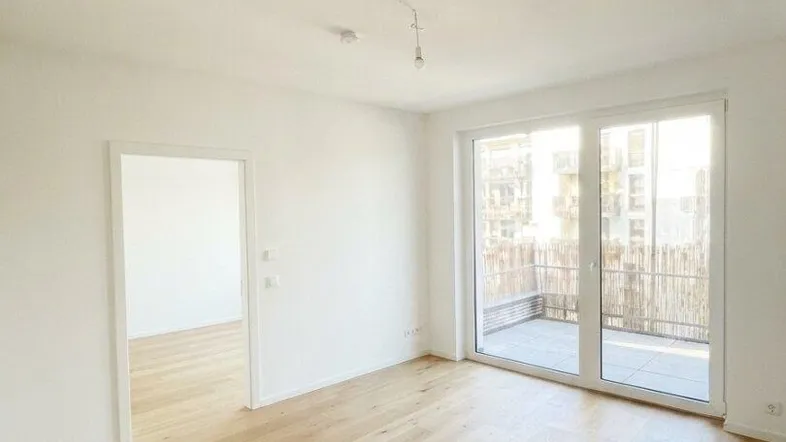 Helles, leeres Zimmer mit Holzboden und Zugang zu einem Balkon, bereit zur individuellen Gestaltung.