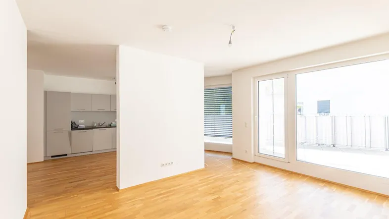 Helles Wohnzimmer mit Parkettboden und Zugang zu einer großen Terrasse, angrenzend an eine moderne Küche.