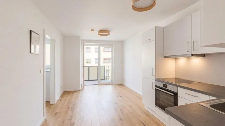 Heller offener Wohnbereich mit integrierter Küche, Holzboden und Zugang zu einem Balkon.