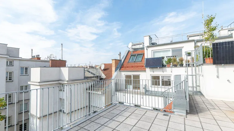 Geräumige Dachterrasse mit Fliesenboden und Blick auf die umliegenden Gebäude und den Himmel.