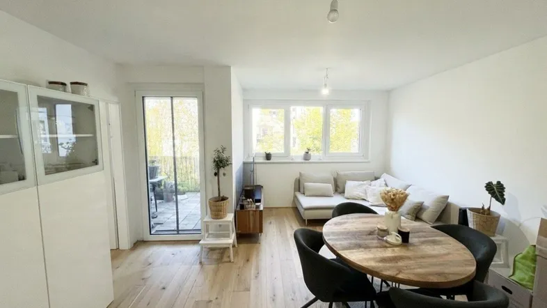 Helles Wohn- und Esszimmer mit Holzboden, Zugang zum Balkon und moderner Einrichtung.