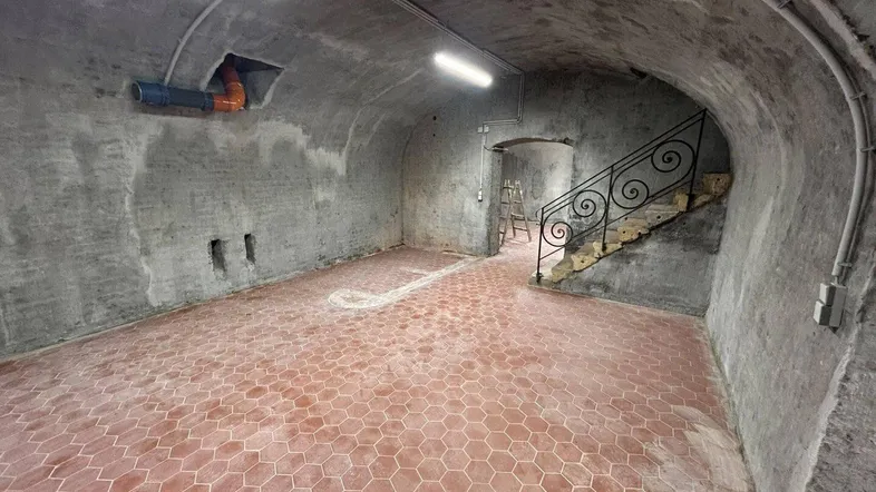 Geräumiger Kellerraum mit gewölbter Decke, Terrakotta-Fliesenboden und einer Treppe mit schmiedeeisernem Geländer.