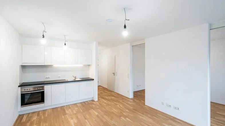 Moderne Küchenzeile mit weißen Schränken, dunkler Arbeitsplatte und Holzboden in einem hellen Raum.
