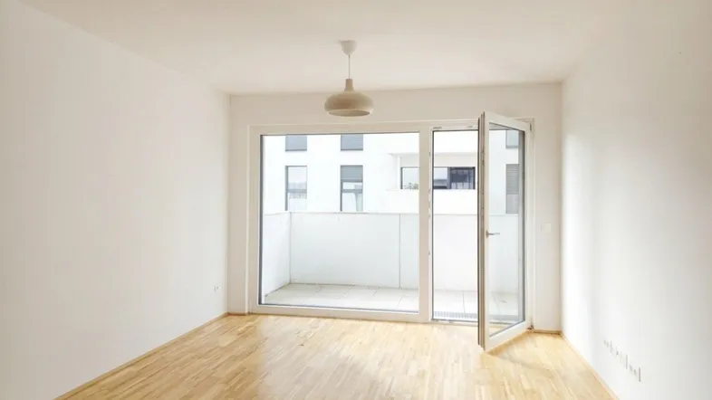 Helles Wohnzimmer mit Parkettboden und Zugang zu einem Balkon, bereit für die Einrichtung.