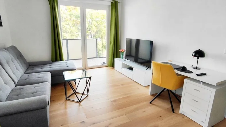 Helles Wohnzimmer mit modernem Sofa, Schreibtisch und Zugang zum Balkon.