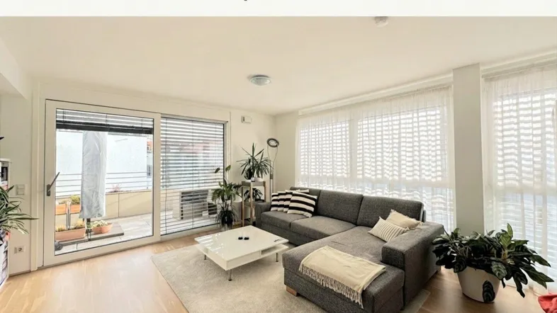 Helles Wohnzimmer mit modernem Sofa, Holzboden und Zugang zu einem sonnigen Balkon.