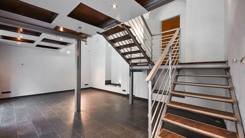 Geräumiger Gewerberaum mit dunklen Fliesen, offener Treppe und moderner Deckenbeleuchtung.