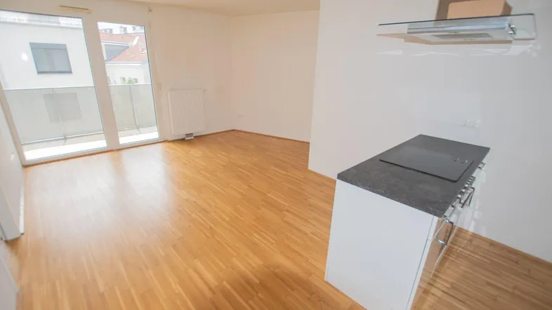 Heller Wohnbereich mit Parkettboden, Zugang zum Balkon und integrierter Küchenzeile.