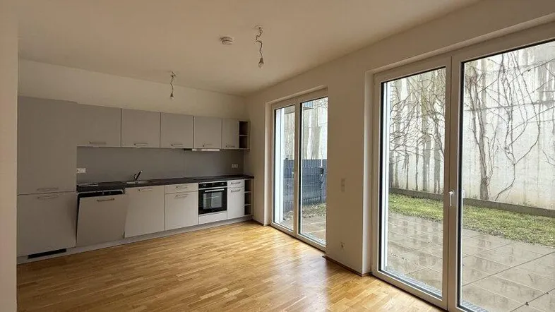 Heller offener Wohnbereich mit integrierter Küche, Parkettboden und Zugang zur Terrasse.