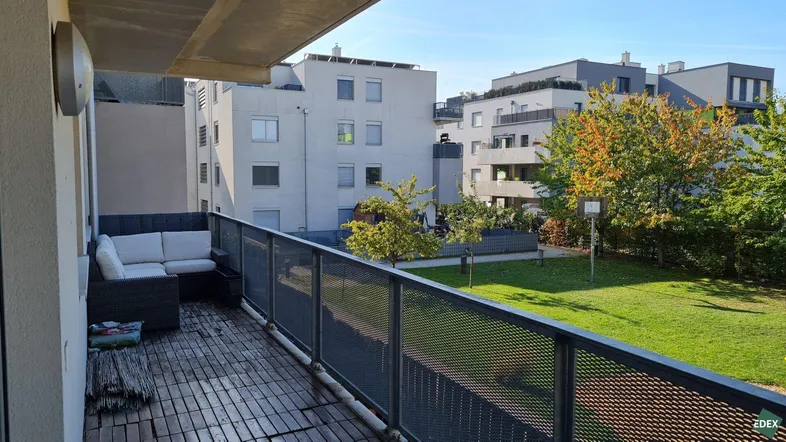 Geräumiger Balkon mit Sitzgelegenheiten und Blick auf die grüne Gemeinschaftsfläche und moderne Gebäude.