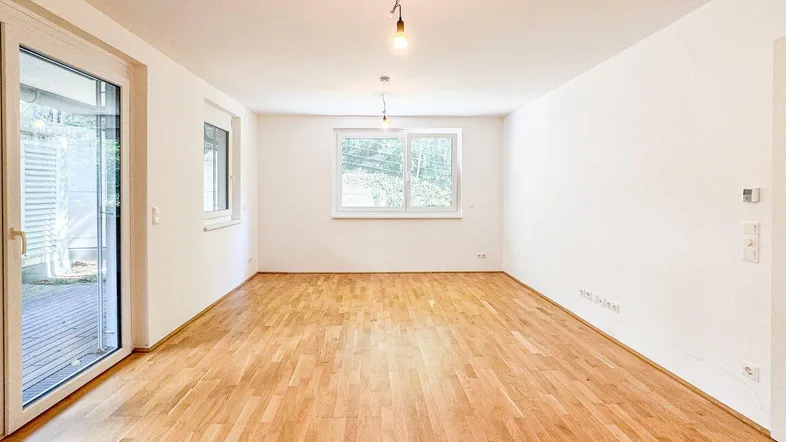 Helles, leeres Zimmer mit Parkettboden und Zugang zu einem Außenbereich durch große Terrassentüren.