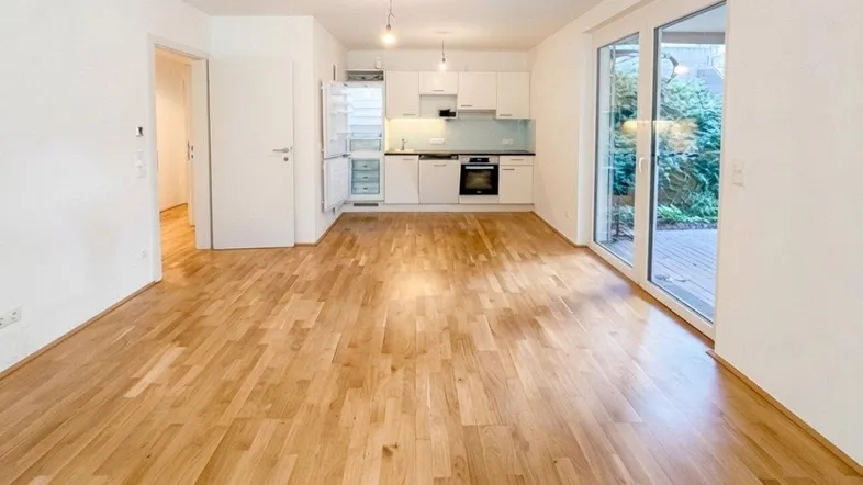Heller offener Wohnbereich mit Parkettboden und integrierter Küche, bietet Zugang zur Terrasse.