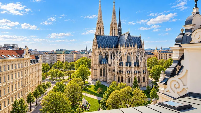 Panoramablick über Wien mit der Votivkirche und umliegenden Gebäuden unter blauem Himmel.