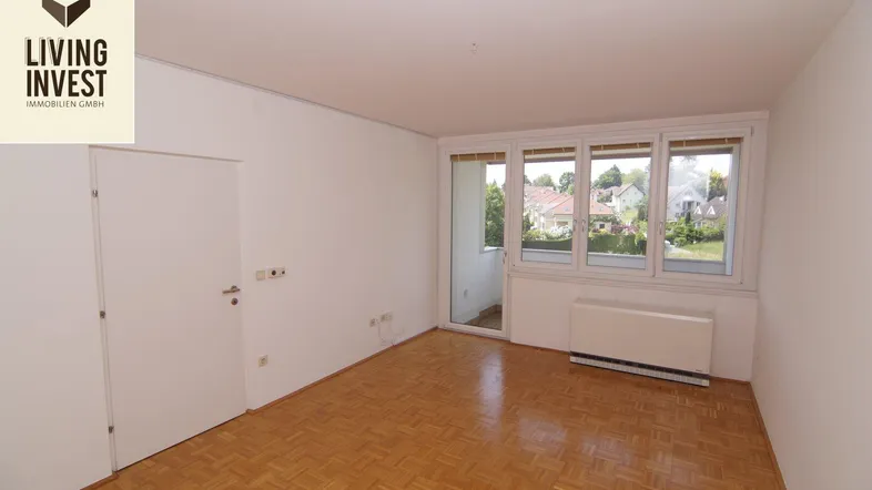 Helles Zimmer mit Parkettboden und großen Fenstern, die einen Blick ins Grüne bieten.