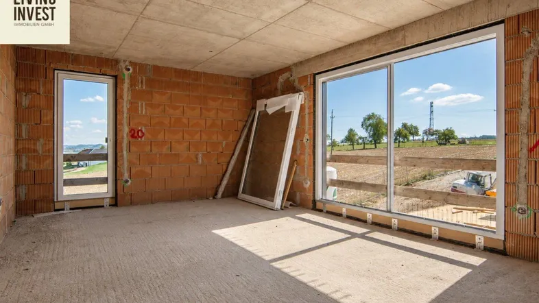 Unfertiger Innenraum eines Neubaus mit großen Fenstern und weitem Blick ins Grüne.