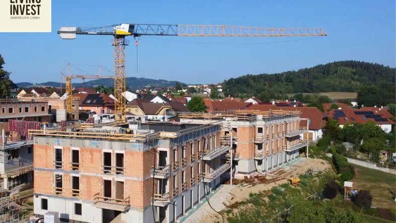 Luftaufnahme einer Baustelle mit mehreren im Bau befindlichen Gebäuden und Kränen in ländlicher Umgebung.