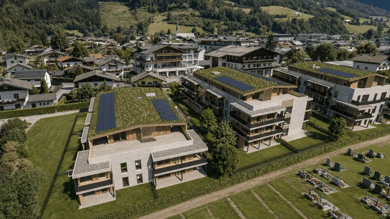 Luftaufnahme moderner Wohngebäude mit begrünten Dächern und Photovoltaikanlagen in einer alpinen Landschaft.
