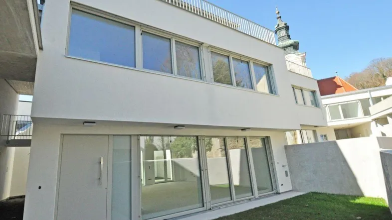 Moderne Neubauwohnung mit großzügigen Glasfronten und direktem Zugang zu einer kleinen Rasenfläche.