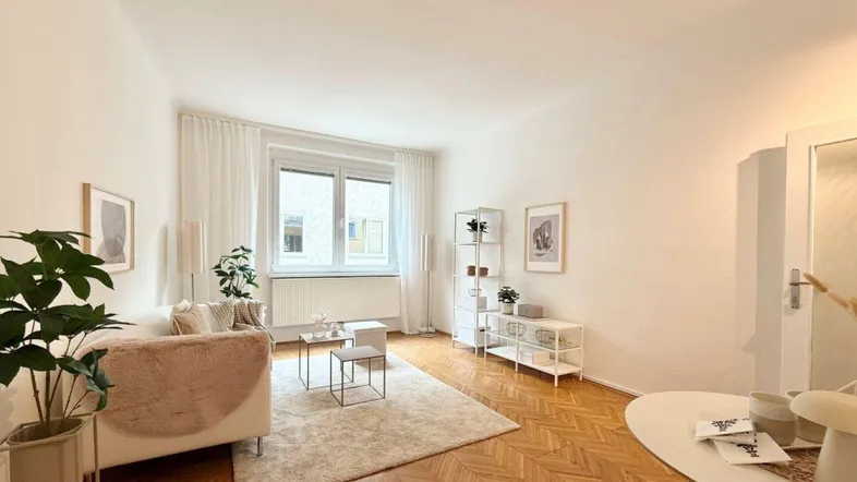 Geräumiges Wohnzimmer mit Fischgrätparkett, weißem Sofa und minimalistischer Einrichtung.
