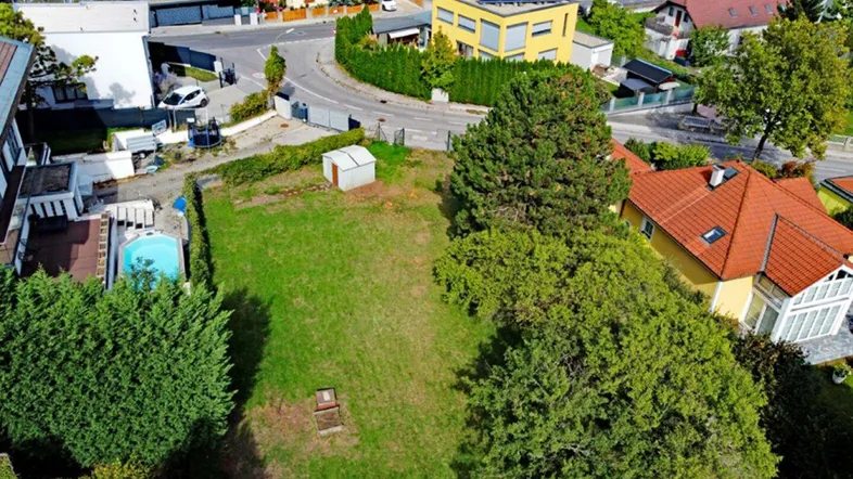 Luftaufnahme eines unbebauten Grundstücks mit umliegenden Wohnhäusern und einem kleinen Schuppen.