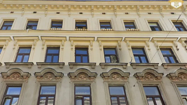 Fassade eines Altbaus mit dekorativen Fensterrahmen und Stuckelementen unter blauem Himmel.