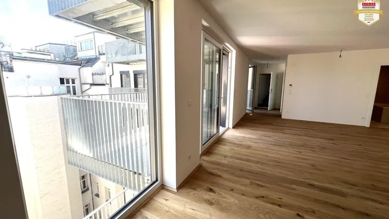Helles, unfurniertes Zimmer mit Holzboden und Zugang zu einem Balkon in einem Neubau.